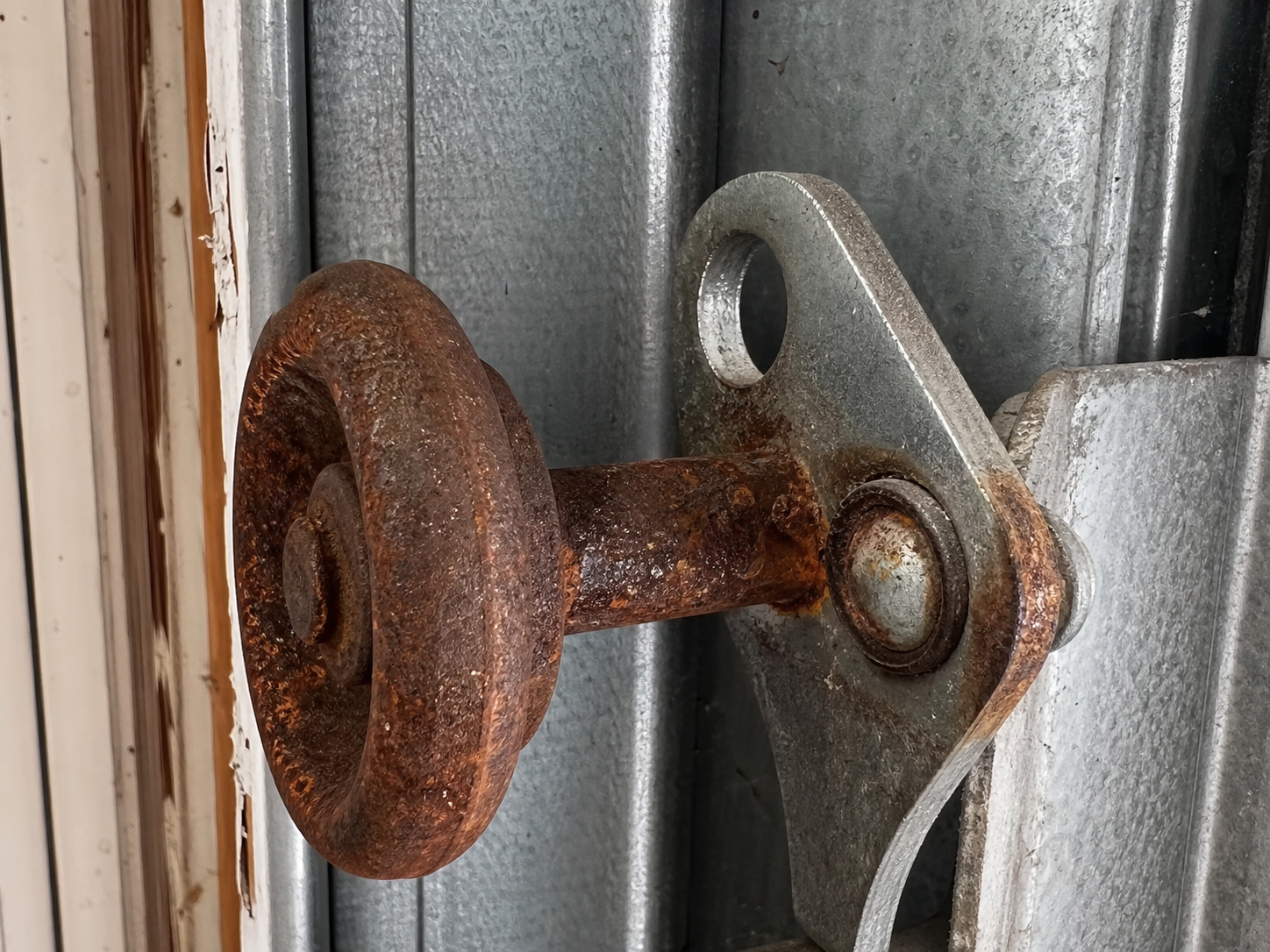 Close-up of corroded steel roller and damaged roller stem on a residential garage door track in the north suburbs of Illinois, showing rust and surface oxidation from prolonged summer humidity exposure