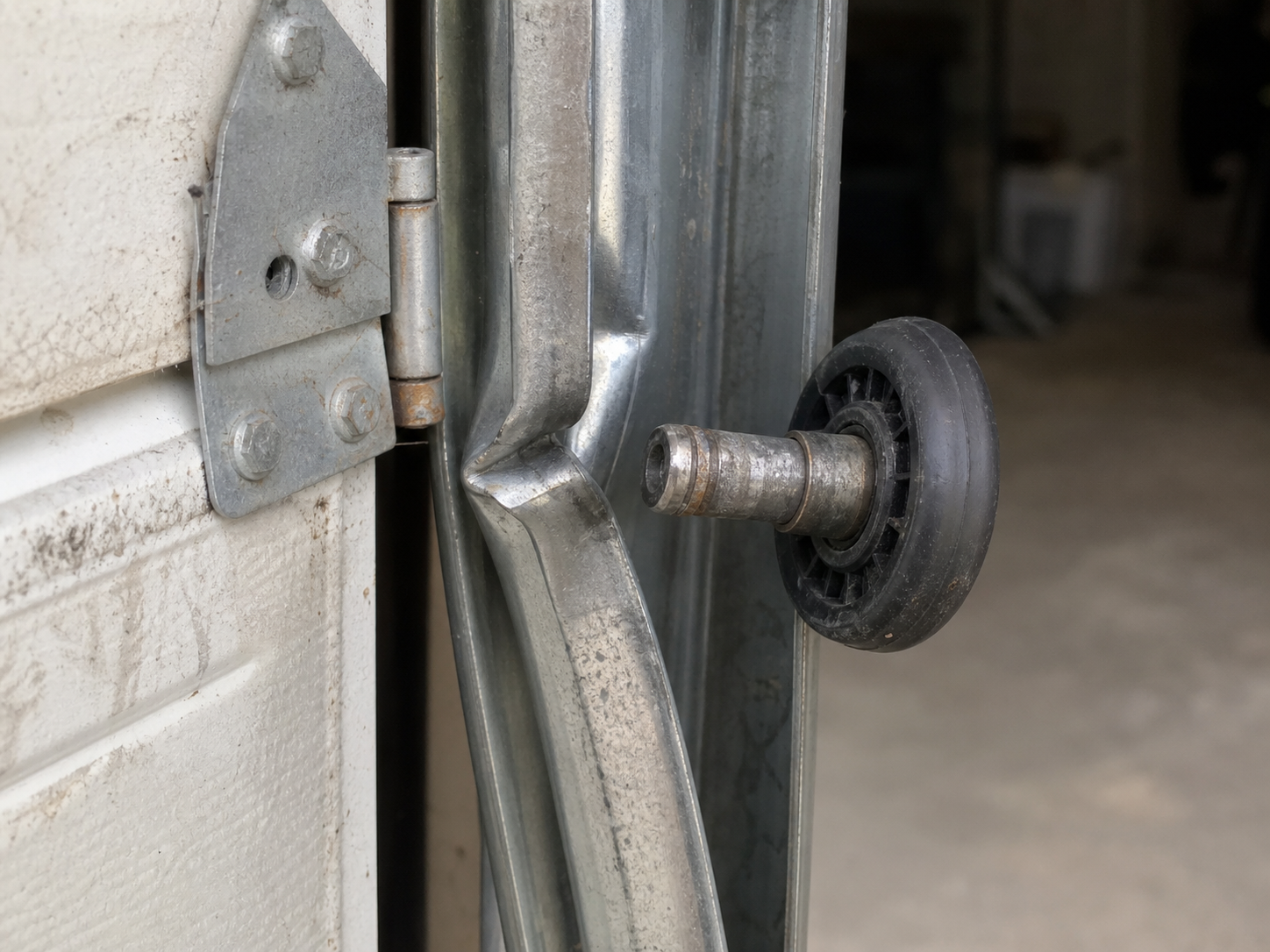 Close-up of a garage door roller stem popped out of a bent vertical track with the panel edge dropped and leaning